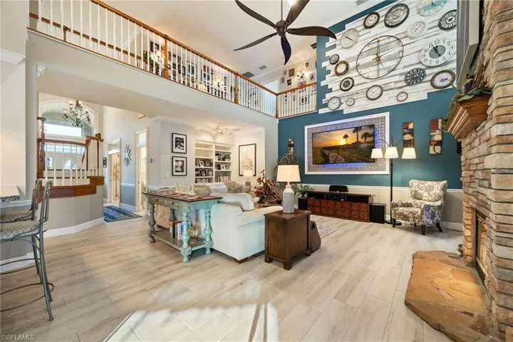 Living area featuring ceiling fan with notable chandelier, ornate columns, wood finished floors, a high ceiling, and baseboards