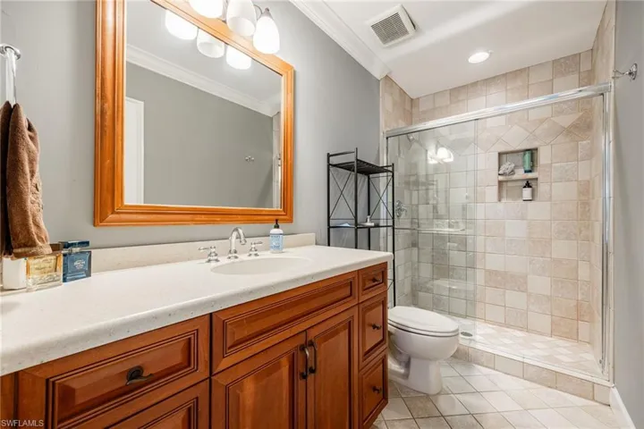 Full bath featuring a shower stall, vanity, ornamental molding, visible vents, and toilet