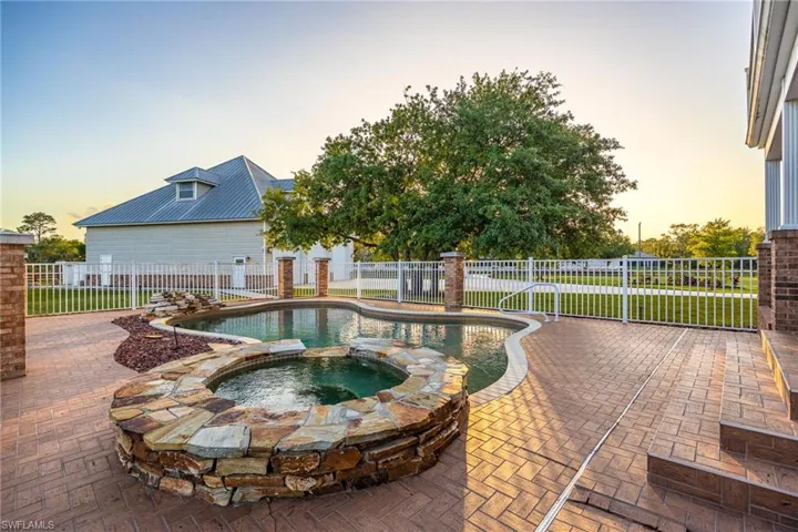 Pool at dusk featuring a pool with connected hot tub, a patio area, and fence