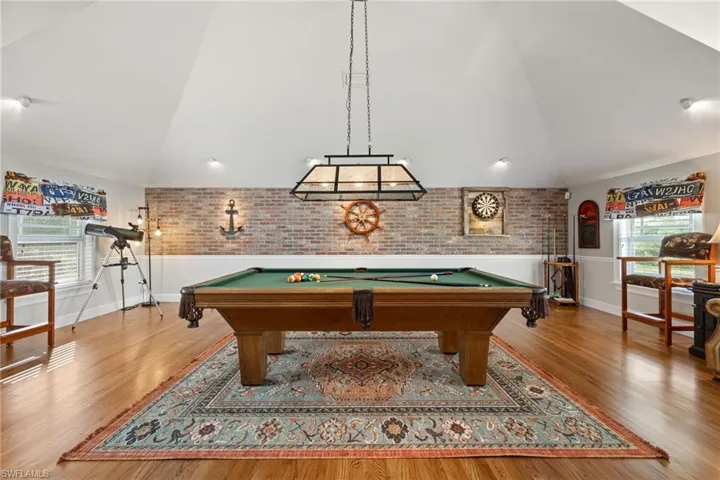 Rec room featuring brick wall, pool table, high vaulted ceiling, and wood finished floors
