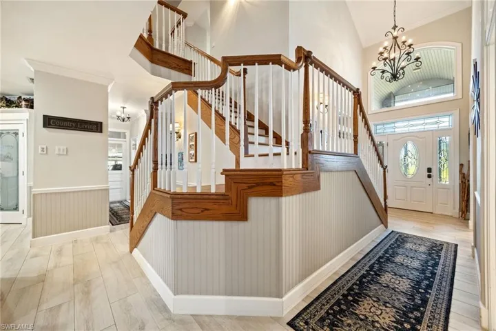 Foyer entrance with high vaulted ceiling, a notable chandelier, a wainscoted wall, and stairway