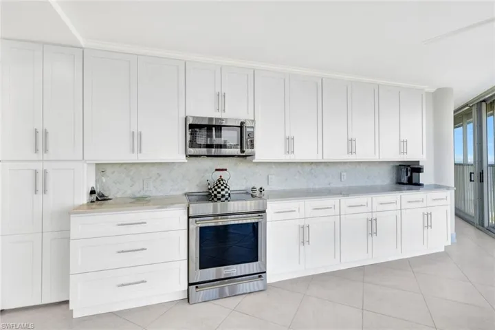 Kitchen featuring tasteful backsplash, appliances with stainless steel finishes, light tile patterned flooring, and white cabinets
