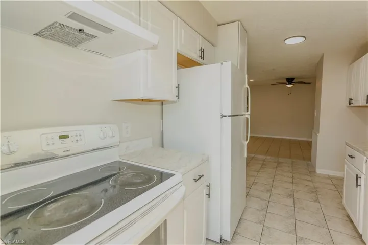 Kitchen featuring white appliances, solid surface countertops, white cabinetry with black hardware, and tile flooring