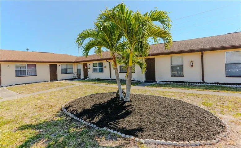 Exterior stucco facade with multiple entry doors, brown shingle roofing, and white-framed windows