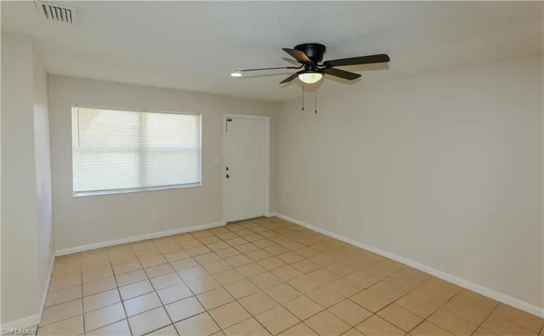 Living area featuring tile flooring, neutral wall paint, a ceiling fan with light fixture, a window with blinds, and a white paneled door