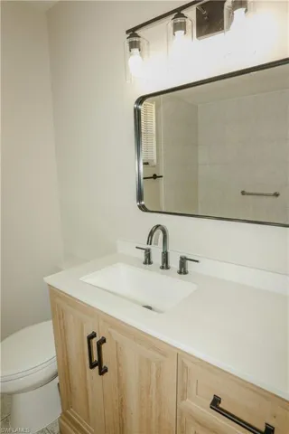Bathroom vanity featuring a light wood-finish cabinet with black hardware, a white countertop, an undermount sink, and a black faucet