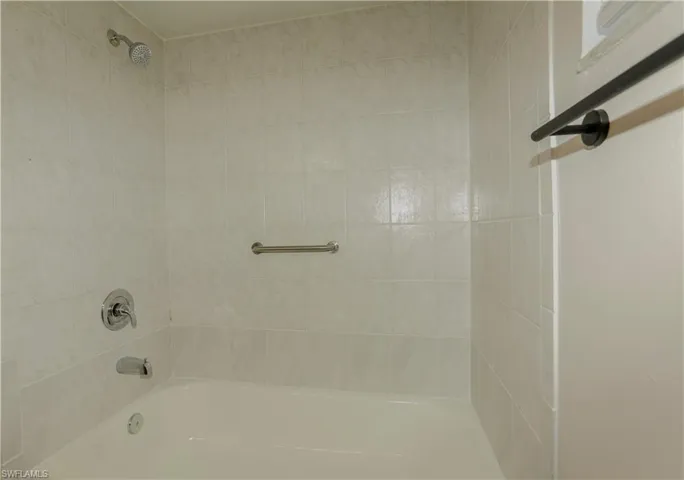 Bathtub with white tile surround, chrome showerhead, and matching fixtures