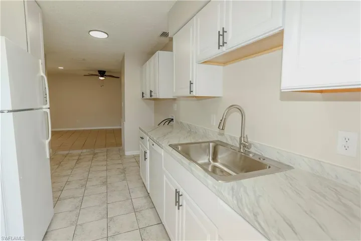 Kitchen featuring white cabinetry, a stainless steel sink with a gooseneck faucet, light-toned countertops, and tiled flooring