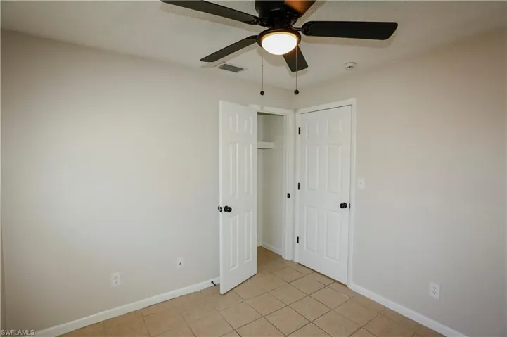 Interior room featuring neutral wall tones, square tile flooring, a dark-toned ceiling fan with integrated lighting, and a closet with a built-in shelf