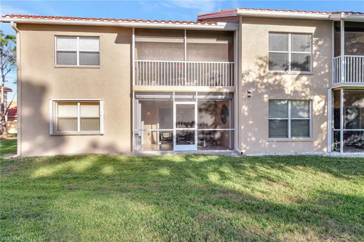 Rear view of property featuring a tiled roof, a lawn, and stucco siding