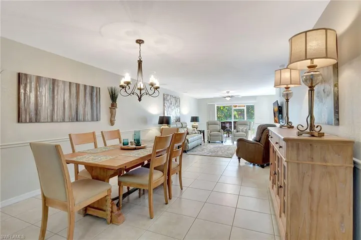 Dining room with ceiling fan with notable chandelier, baseboards, and light tile patterned floors