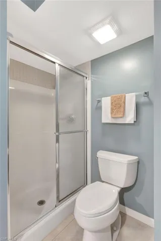 Full bath featuring a stall shower, tile patterned flooring, toilet, and baseboards
