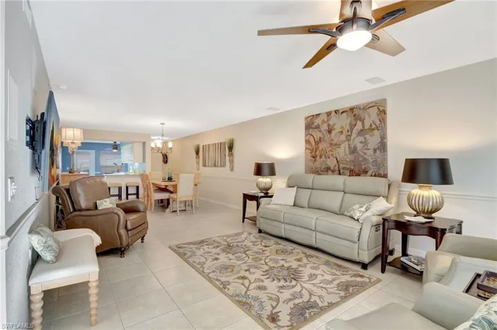 Living room featuring light tile patterned floors, ceiling fan with notable chandelier, visible vents, and baseboards