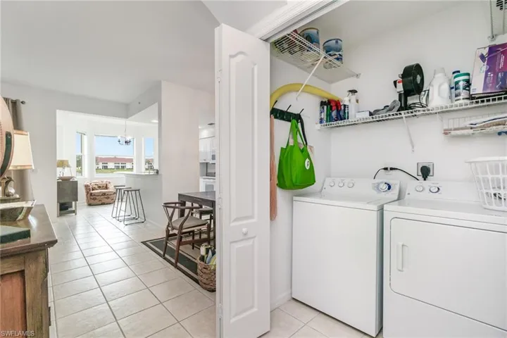 Laundry room with light tile patterned flooring, washing machine and dryer, and a chandelier