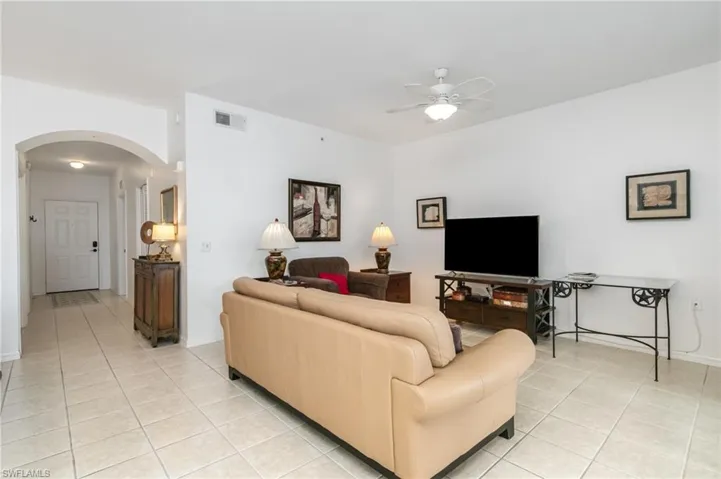 Living room featuring arched walkways, light tile patterned floors, a ceiling fan, and baseboards