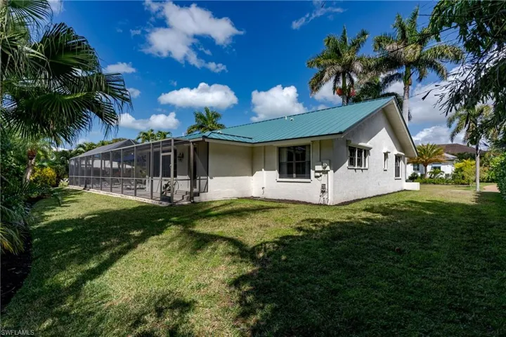 Rear view of property featuring a sunroom, a yard, a lanai, stucco siding, and a metal roof