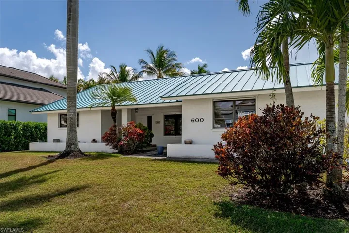 Ranch-style house with a standing seam roof, stucco siding, and a front lawn