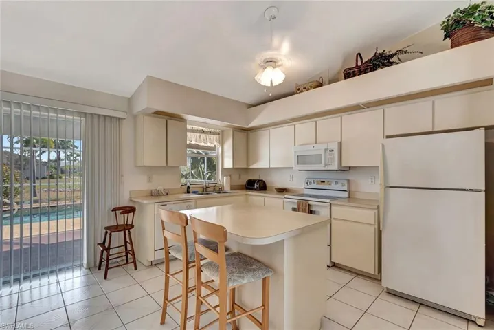 Kitchen with white appliances, light countertops, light tile patterned floors, a kitchen bar, and a kitchen island