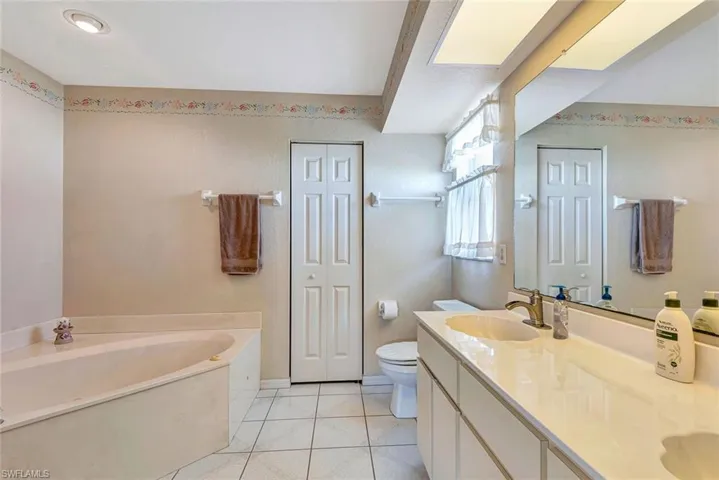 Bathroom with a closet, double vanity, a bath, and light tile patterned flooring