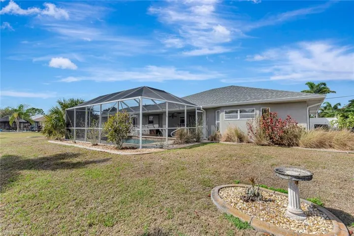 Back of property with a lawn, a sunroom, an outdoor pool, glass enclosure, and stucco siding