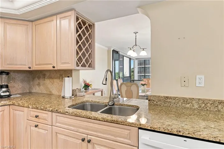 Kitchen featuring double basin stainless steel sink, granite countertops, light wood-finish cabinetry, and a built-in wine rack