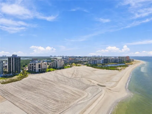 Expansive beachfront property featuring a sandy shoreline, coastal waters, and a distant city skyline