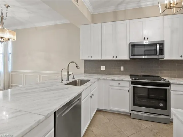 Kitchen featuring stainless steel appliances, ornamental molding, white cabinets, hanging lights, and light stone counters