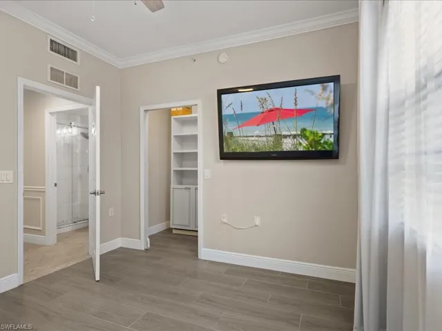 Unfurnished bedroom featuring wood tiled floors, a walk in closet, crown molding, and a ceiling fan