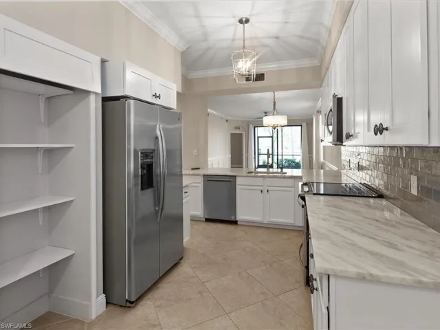 Kitchen featuring stainless steel appliances, white cabinets, ornamental molding, hanging lights, and light tile patterned flooring