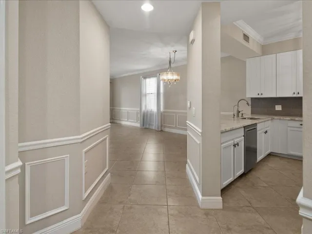 Kitchen with a decorative wall, wainscoting, white cabinetry, crown molding, and a chandelier