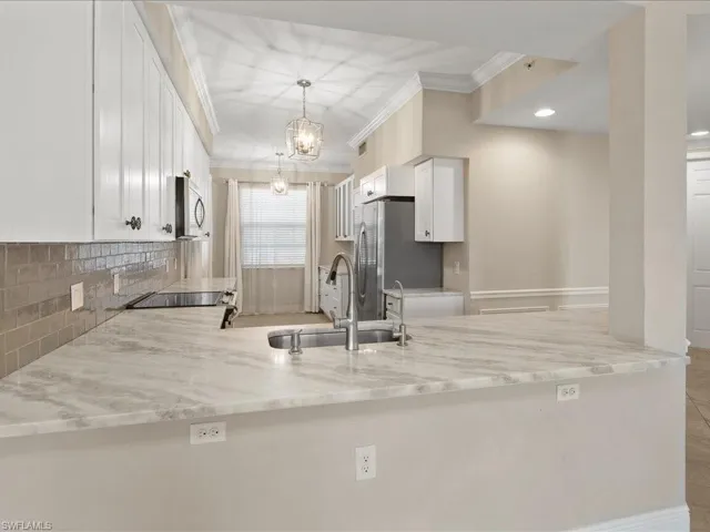 Kitchen featuring white cabinetry, ornamental molding, a peninsula, light stone countertops, and stainless steel appliances