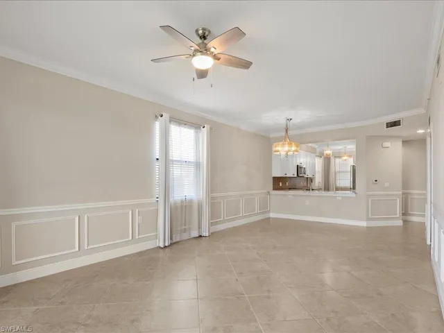 Unfurnished room with a decorative wall, wainscoting, crown molding, a ceiling fan, and a chandelier