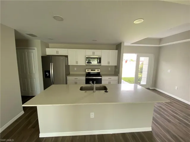 Kitchen with white cabinetry, appliances with stainless steel finishes, a center island with sink, dark wood-type flooring, and recessed lighting