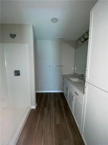 Full bath featuring a shower, vanity, and dark wood-type flooring