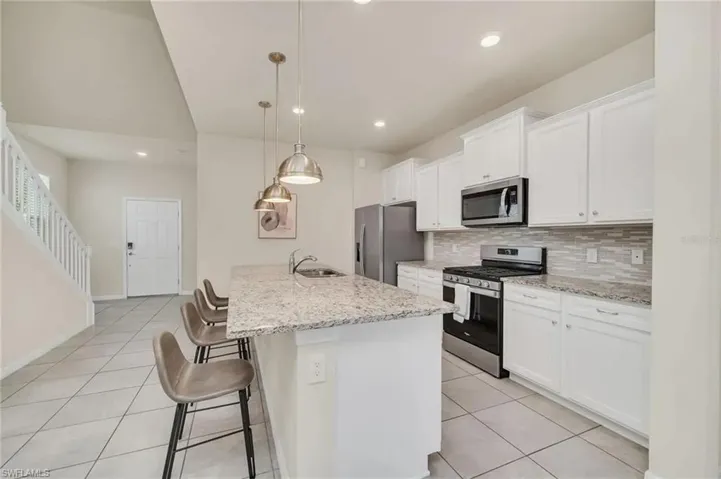 Kitchen featuring a kitchen bar, stainless steel appliances, white cabinets, light tile patterned floors, and tasteful backsplash