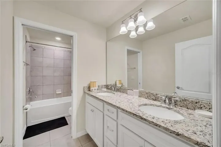 Full bathroom with double vanity, light tile patterned floors, and shower / bathtub combination