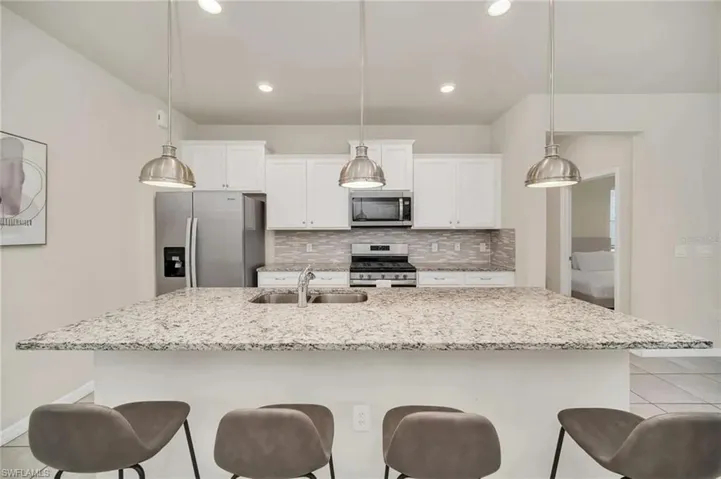 Kitchen with stainless steel appliances, a breakfast bar, white cabinets, and a center island with sink
