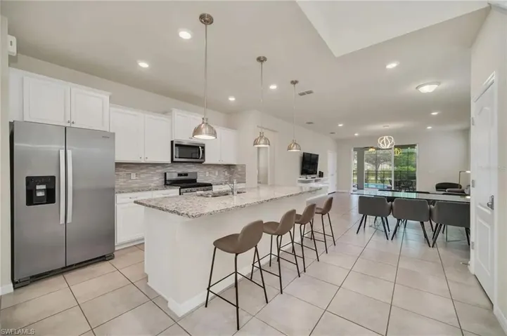 Kitchen with stainless steel appliances, light stone countertops, a center island with sink, a breakfast bar, and white cabinets