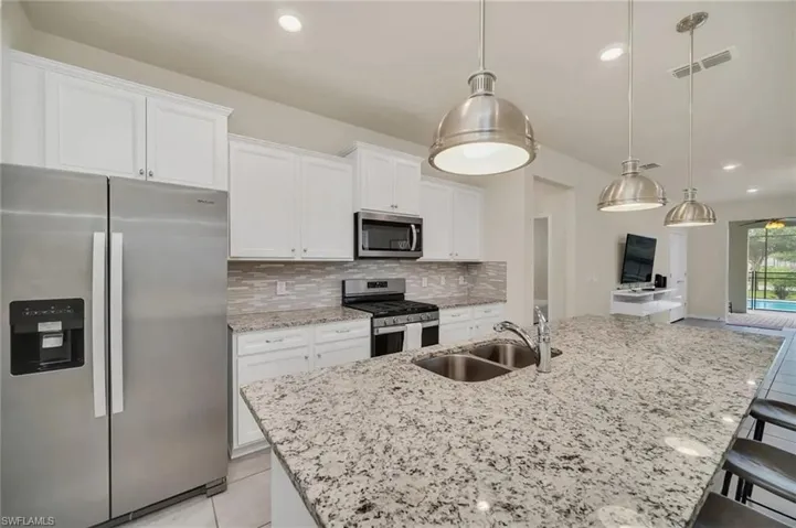 Kitchen featuring stainless steel appliances, a breakfast bar area, white cabinetry, light stone countertops, and a center island with sink