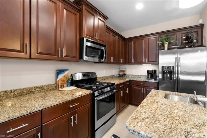 Kitchen featuring appliances with stainless steel finishes, light tile patterned flooring, a sink, and light stone counters
