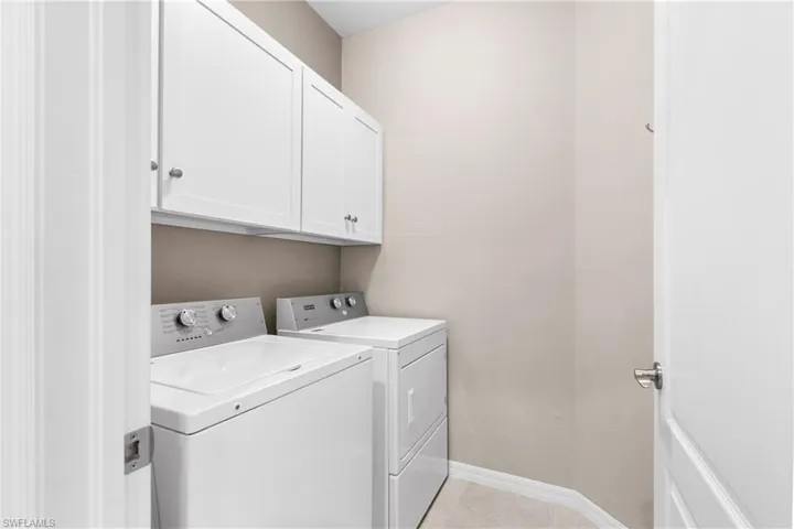 Laundry area featuring washer and dryer, cabinet space, baseboards, and light tile patterned floors