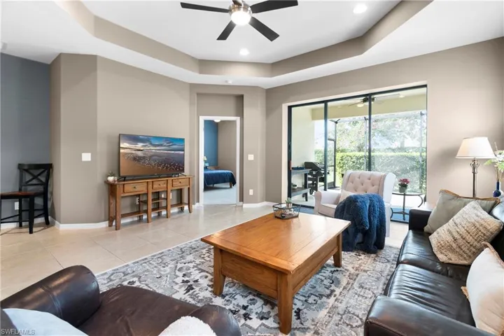 Living room featuring light tile patterned floors, a tray ceiling, a ceiling fan, and baseboards