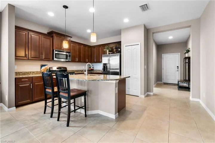 Kitchen with light stone counters, a kitchen island with sink, stainless steel appliances, visible vents, and decorative light fixtures