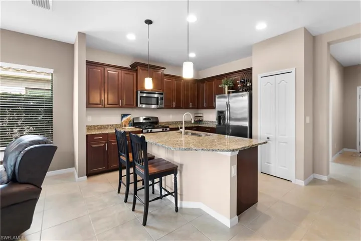 Kitchen featuring light stone counters, a center island with sink, stainless steel appliances, hanging light fixtures, and a sink