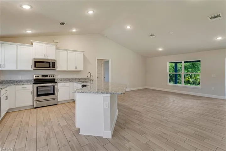 Kitchen featuring visible vents, appliances with stainless steel finishes, a sink, a peninsula, and lofted ceiling