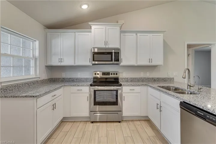 Kitchen with white cabinetry, appliances with stainless steel finishes, a sink, and vaulted ceiling