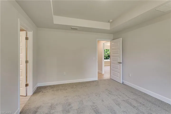 Spare room featuring light colored carpet, a tray ceiling, visible vents, and baseboards