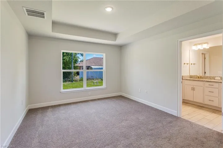 Unfurnished bedroom featuring baseboards, light carpet, a raised ceiling, and visible vents