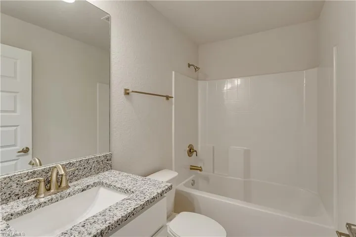 Full bathroom with toilet, a textured wall, shower / tub combination, and vanity