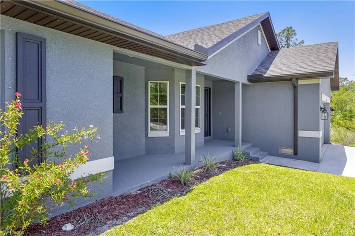 View of front of home with a shingled roof, covered porch, stucco siding, and a front lawn